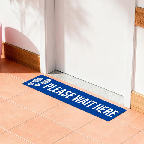 Five Piece Please Wait Here Floor Sign Kit 26 By 6 Inches Self Adhesive Waterproof Vinyl, Durable Social Distancing Markers For Queues And Waiting Areas, Multipack Signage For Busy Shops. Blue floor sign on tiled floor near a door