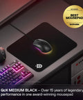 QcK Medium Gaming Mouse Pad With Non Slip Silicone Rubber Base For Peak Tracking And Pro Grade Game Ready Sensor Performance 320 By 270 mm For FPS MOBAs RTS MMO showing mouse on desk setup