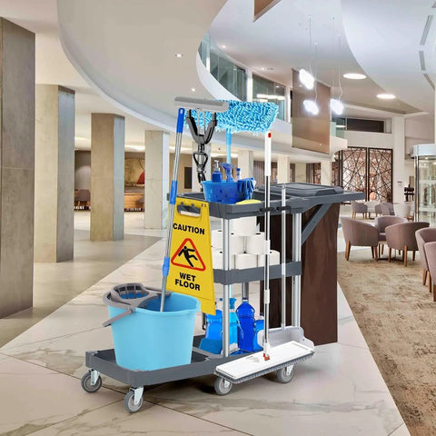Built Different Heavy Duty Three Shelf Janitorial Cart With Roller Wheels And Secure Protective Cover Includes Generous Vinyl Storage Bag For Top Shelf Housekeeping Performance In Offices Hotels And Schools with cleaning supplies in a hotel lobby.