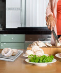 Person chopping mushrooms with an On The Go Pocket Scale With 2000g Capacity And 0.1g Precision nearby on kitchen counter.
