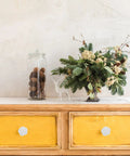 Wooden dresser with yellow drawers featuring white ceramic rose flower cabinet pull handles with screws, elegant retro design.
