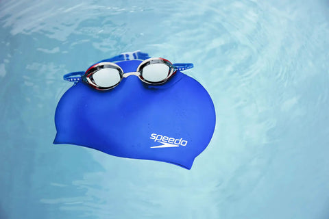 Blue swim cap with goggles in a pool; Go-To Unisex Silicone Swim Cap For Adults, No-Snag, Stretchy, Hair-Friendly Cap That Protects Hair From Chlorine