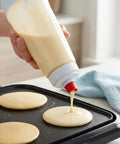 All In One Pancake Batter Dispenser With BlenderBall and Wire Whisk in use on griddle, pouring batter onto pan