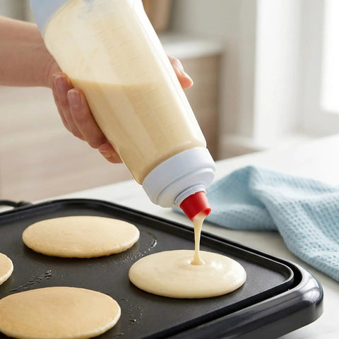 All In One Pancake Batter Dispenser With BlenderBall and Wire Whisk in use on griddle, pouring batter onto pan