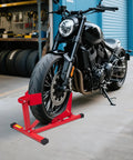 Heavy Duty Motorcycle Wheel Chock And Front Tire Stand For 17 To 21 Inch Rigs Adjustable 1500 Lb Capacity Red Steel Trailer Stand For Easy Bike Parking And Safer Rides securing a motorcycle front tire in a garage setting