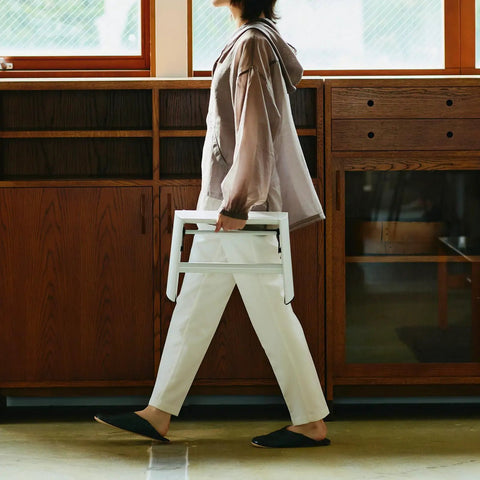 Woman carrying a white step ladder with self standing foldable design in a home setting