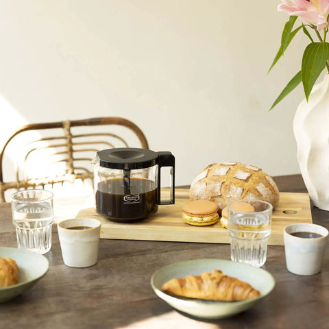 1.25L Glass Carafe for KBG Brewers, Clear Black Version next to bread and pastries on a wooden table, sunlight streaming in