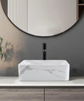 Rectangular Above Counter Vessel Sink 16 By 12 Inch Porcelain Ceramic Bathroom Sink With Faucet And Pop Up Drain Included White And Black Finish Stain Resistant Sleek Modern Vanity Upgrade For Your Bathroom displayed on a wooden vanity against a dark wall.