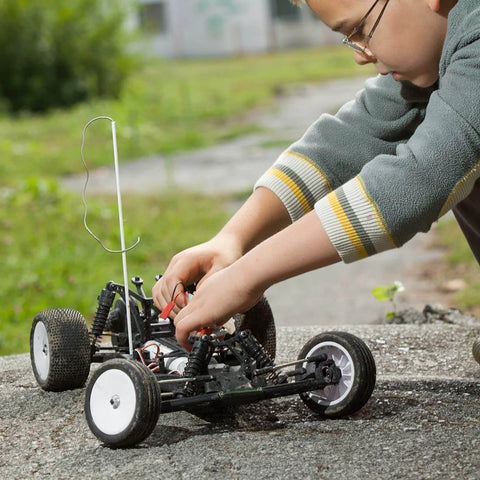 Child adjusting remote-controlled car outdoors on rough surface