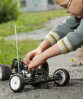 Child adjusting RC car outdoors on a paved surface, focusing on mechanical parts and wiring for precision modeling.