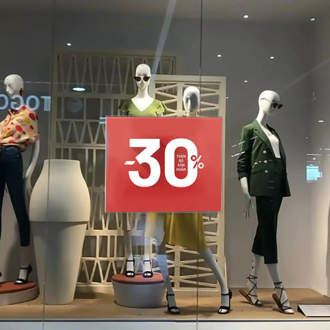 Storefront mannequins with -30% sale sign. Fashion displayed in glass showcase, shopping mall environment.