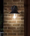 Orion Outdoor Solar Wall Light With 150 Lumen Warm White LED At 2700K on brick wall at night, black resin sconce