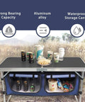 Aluminum Folding Camp Table With Built In Storage Compartment, Lightweight Height Adjustable Outdoor Kitchen Table For Tailgating, Backyards, BBQ, And Picnics, Black with drinks and snacks on top in a field setting.