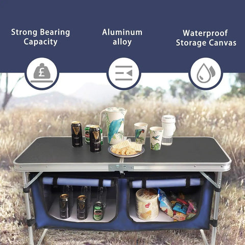 Aluminum Folding Camp Table With Built In Storage Compartment, Lightweight Height Adjustable Outdoor Kitchen Table For Tailgating, Backyards, BBQ, And Picnics, Black with drinks and snacks on top in a field setting.