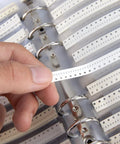 Hand selecting a strip from 0402 Capacitor Kit With 4000-Piece Grab-And-Go Assortment Booklet, showcasing clear labeling in a binder.