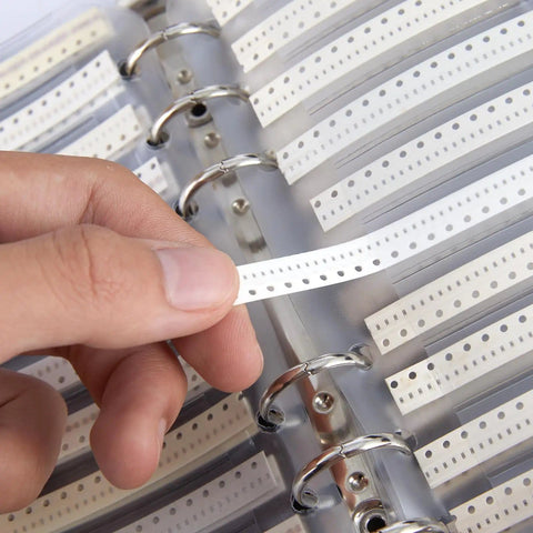 Hand selecting a strip from 0402 Capacitor Kit With 4000-Piece Grab-And-Go Assortment Booklet, showcasing clear labeling in a binder.