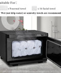 Pro 8L Towel Warmer For Salon And Spa showing open door with 8 rolled towels inside, black metal design in spa setting.
