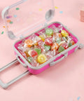Pink mini suitcase party favor box with wheels, open lid, filled with wrapped candies