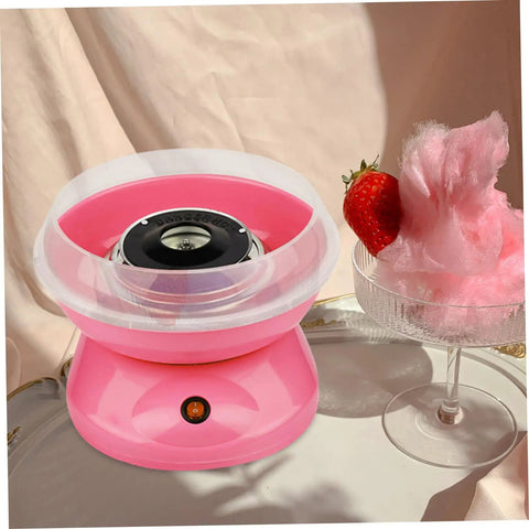 Pink cotton candy machine with a clear guard cover next to a bowl of pink cotton candy and strawberry, tabletop view.