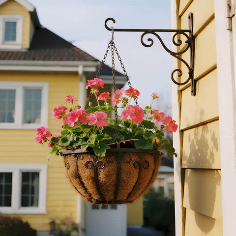 Hanging basket with pink flowers on black metal bracket against yellow house exterior
