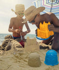 Kids playing with 7 Piece Beach Sand Toys Set with buckets, shovels, rakes, and castle sand molds at the beach. Durable plastic.