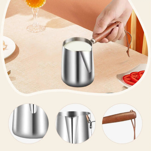 Stainless Steel Milk Warmer And Frother Pot With Wooden Handle Barista Grade Multipurpose Milk Frother Cup For Home Or Cafe 900ml Capacity Great For Latte Art Coffee Tea And Melting Chocolate with milk poured inside, shown on a table.