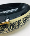 Sleek oval ceramic vessel sink with matte gold trim and intricate black floral design for luxury bathroom use.