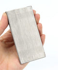 A hand holding a steel rectangle wedge, part of a Six Pack Of Steel Flange Wedges With Beveled Right Angle Shims for welding machines.