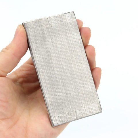 A hand holding a steel rectangle wedge, part of a Six Pack Of Steel Flange Wedges With Beveled Right Angle Shims for welding machines.