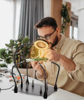Helping Hands Soldering Clamp Station with 6X LED Magnifying Lamp, person soldering a PCB with flexible metal arms and weighted base.