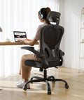 Person seated on ergonomic desk chair for long hours with high back and plush lumbar support, flip-up armrests, in home office setting.