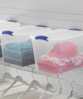 27 Quart Medium Clear Plastic Storage Bin With Heavy Duty Latching Lid And Sturdy Handles For Garage And Closet Organization stacked on shelves with clothing inside.