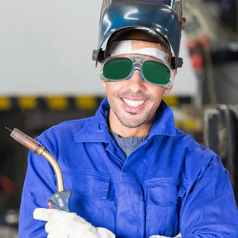 Built Different Welding Safety Goggles With Top Shelf Impact Resistance And Dust Splash Proof Black Gray Lenses For Heavy Duty Shop Work And Everyday Welder Gear worn by smiling worker in blue jacket.