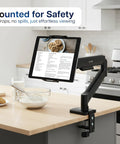 Level Up Your Workspace With This Height Adjustable Counterbalance Desk Mount For Tablets And 15 6 Inch Two In One Laptops Slick Spring Loaded Arm Rock Solid Grip Smooth Glide Finish Black mounted on kitchen counter with tablet displaying recipe.