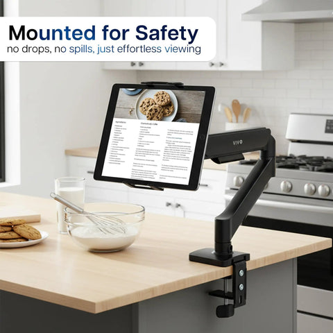 Level Up Your Workspace With This Height Adjustable Counterbalance Desk Mount For Tablets And 15 6 Inch Two In One Laptops Slick Spring Loaded Arm Rock Solid Grip Smooth Glide Finish Black mounted on kitchen counter with tablet displaying recipe.