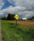 Two Pack Dang Tough Slow Warning Signs Measuring Twelve Inches Square Cut From Heavy Duty Rust Free Aluminum Featuring Vivid Reflective Sheets And Top Shelf Fade Guard Paint For Sure Fire Night Visibility in rural setting.