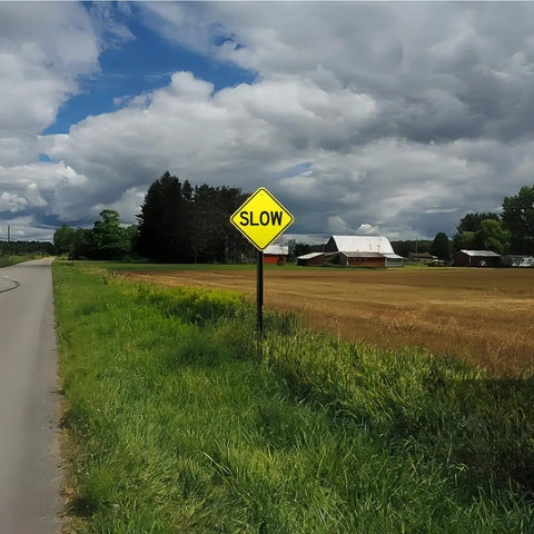 Two Pack Dang Tough Slow Warning Signs Measuring Twelve Inches Square Cut From Heavy Duty Rust Free Aluminum Featuring Vivid Reflective Sheets And Top Shelf Fade Guard Paint For Sure Fire Night Visibility in rural setting.