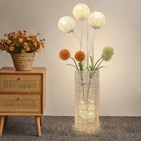 Pastoral LED Floor Lamp With Handwoven Rattan Flower Shade next to wooden dresser in cozy living room setting.