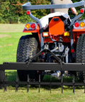 32 Inch Tow Behind Spike Aerator with durable steel tines, hitched to a red tractor on a green lawn, showing deep soil penetration