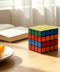 Rubik's Cube on a wooden table next to an open book and orange slices, sunlight streaming through a window.