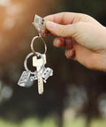 Lightweight Silver Zinc Alloy Travel Themed Keychain For Campers And RV Owners Easy To Carry Gift For Adventurers And Travelers On The Go Perfect For Outdoor Camping And Road Trip Gear being held with a hand outdoors