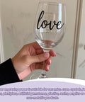 Clear wine glass with black love script, held in hand, side view.
