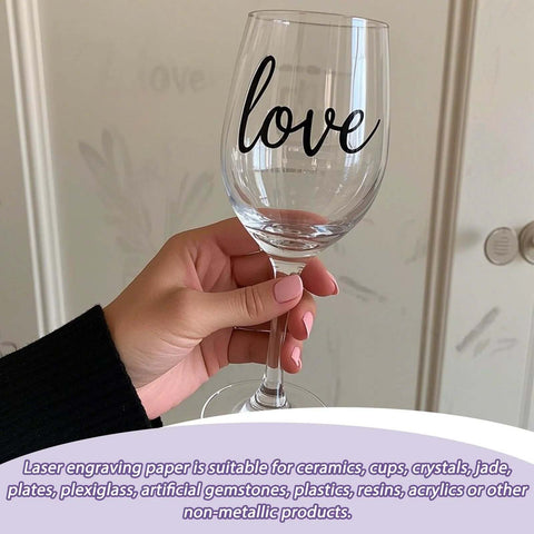 Clear wine glass with black love script, held in hand, side view.