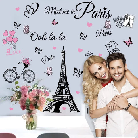 Couple posing with dope Eiffel Tower wall decals set featuring balloons, butterflies on TV wall; removable vinyl stickers decor.