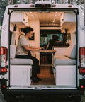 Person working on a laptop inside a van with a cozy design featuring Ultra Slim 12V Led Ceiling Puck Light With Sweet Dimming Controls For Rv Camper Van Trailers Snaps Right Into Tight Spaces High CRI Cozy Glow Heavy Duty Build Road Trip Ready Overhead Lamp Upgrade For Camping Crews Worldwide.