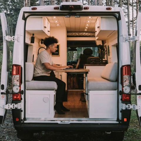 Person working on a laptop inside a van with a cozy design featuring Ultra Slim 12V Led Ceiling Puck Light With Sweet Dimming Controls For Rv Camper Van Trailers Snaps Right Into Tight Spaces High CRI Cozy Glow Heavy Duty Build Road Trip Ready Overhead Lamp Upgrade For Camping Crews Worldwide.