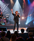 Live band performing on stage with singer, guitarist, bassist, and drummer under colorful stage lights and audience watching.
