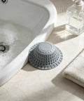 Bathtub Drain Strainer Silicone Bathroom Stopper Fixture in gray positioned beside bubble bath and a towel.