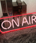 Red and white 'ON AIR' neon sign on a shelf with books in the background