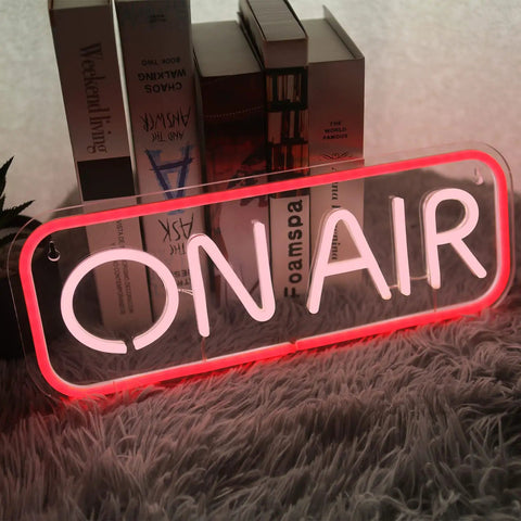 Red and white 'ON AIR' neon sign on a shelf with books in the background